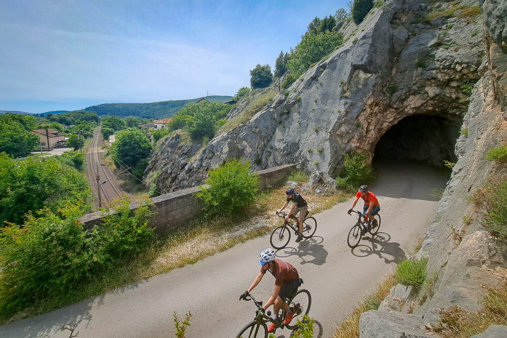 three cyclist on a road above the train tracks